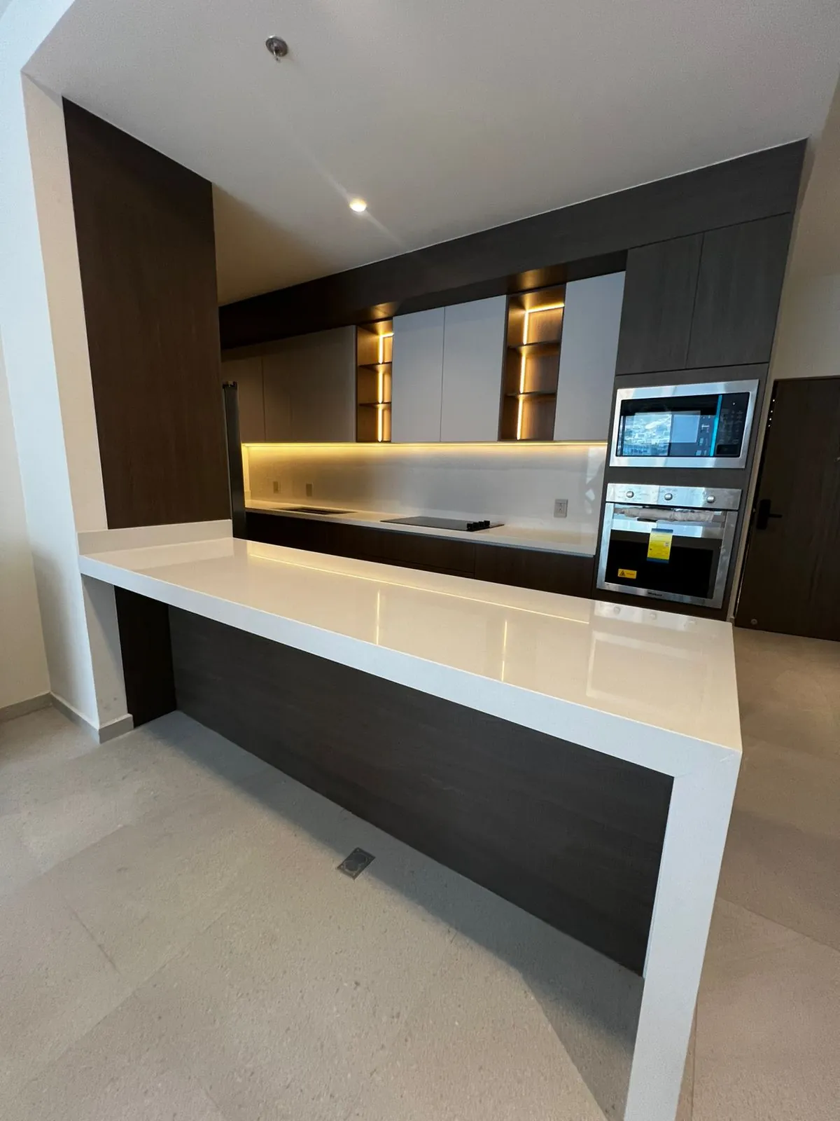 Cocina entregada con gabinetes en tono chocolate, alacenas claras, nichos con luz cálida y barra de cuarzo blanco